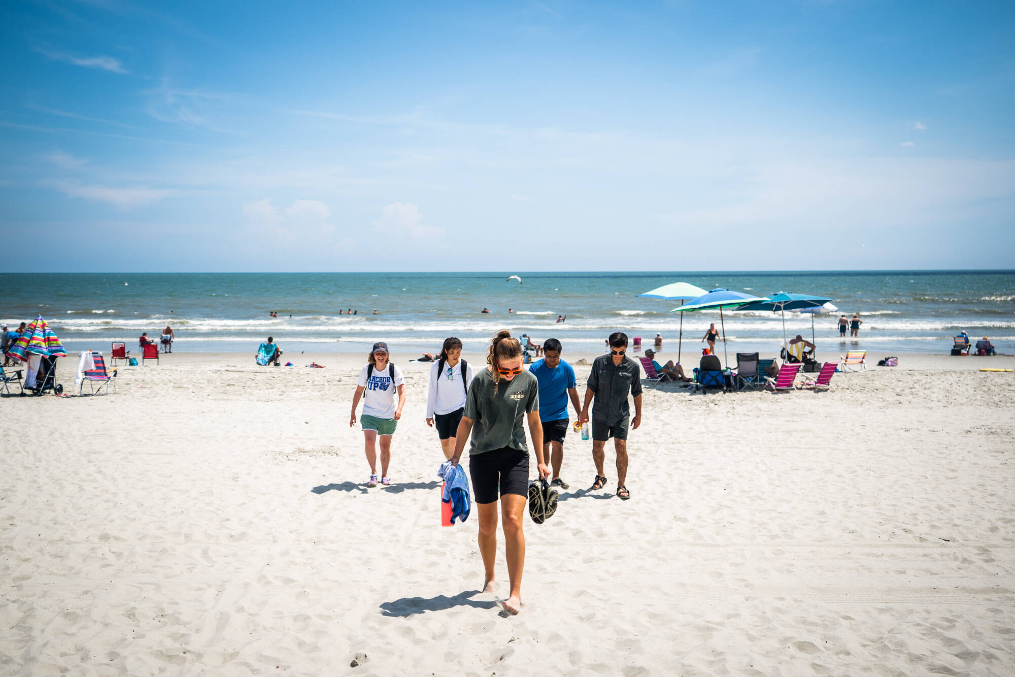 individuals walking away from the water up the sandy shore toward the camera